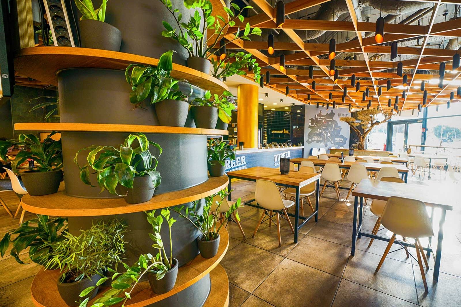 Freundlicher Gastraum mit vielen Pflanzen, Holzgitterdecke und Tischen mit weißen Stühlen. Ein konzipierter Ladenbau in Berlin von confaktum.