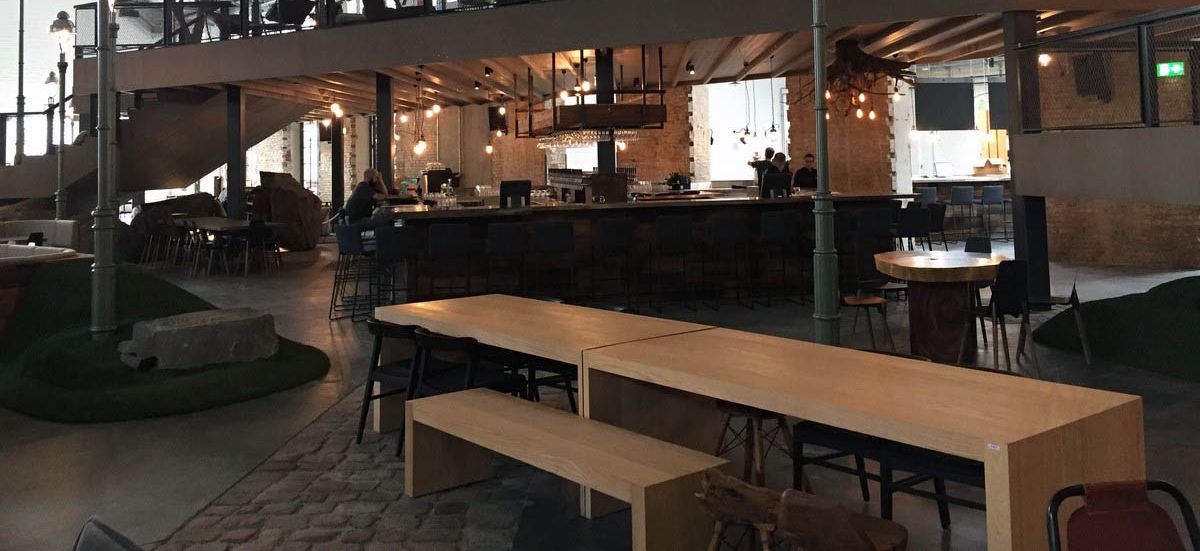 Großer, industriell gestalteter Ladenbau in Berlin mit Bar, Empore und hohen Decken, ausgestattet mit Holzelementen und Metallelementen von confaktum.