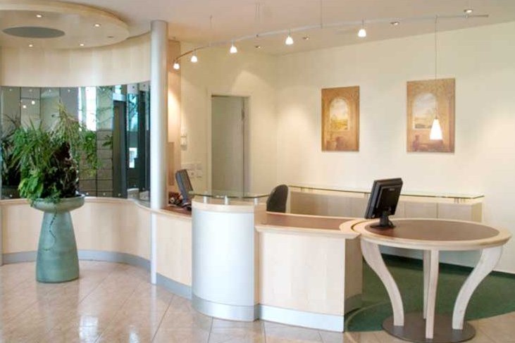 Heller Empfangsbereich mit geschwungenem Tresen, Computern und dezenten Beleuchtungselementen. Ein Ladenbau in Berlin konzipiert von confaktum.